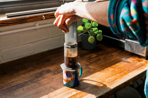 Image of a mans hands and arms pushing down an AeroPress with coffee into a mug
