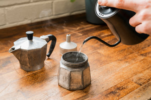 Kettle pouring hot water into a silver Mokapot