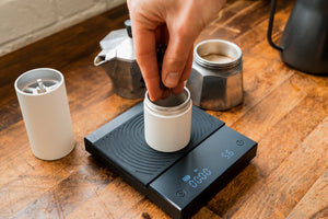 Close up of a hand placing coffee beans into a coffee grinder on a scales set