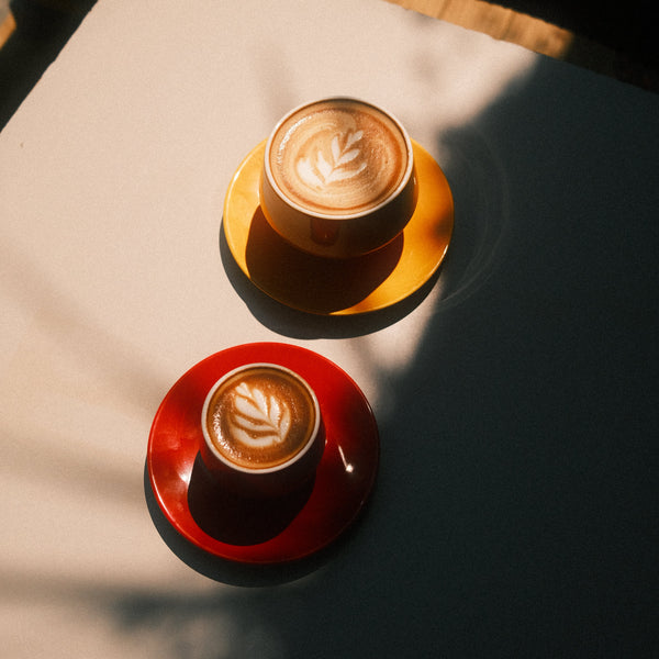 Two cups of goldstone coffee with latte art on a textured surface