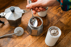 Freshly ground coffee from Small Batch being pushed into a Mokapot with the back of a silver spoon