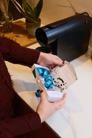 Womens hands opening a Small Batch Coffee Pod package with Morning Mini Machine in background