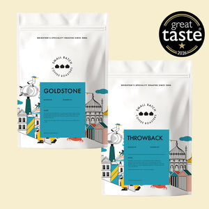 Two white coffee roaster bags from Small Batch Coffee Roasters on a light beige background, one labeled Goldstone and the other labeled Throwback, with a black circular 'great taste 2025' badge in the top right.