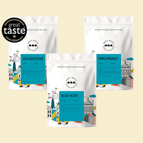 Three stand-up pouches of small Batch Coffee Roasters are arranged on a light beige background, with a black 'great taste 2024' award badge in the top-left corner. The pouches are labeled Goldstone, Blue Note, and Throwback, each featuring a bright teal label and colorful illustrated graphics at the bottom.